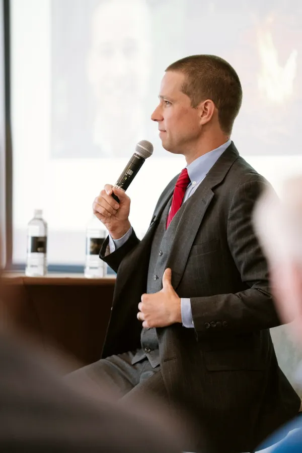 Leroy speaking into a microphone in a three-piece suit